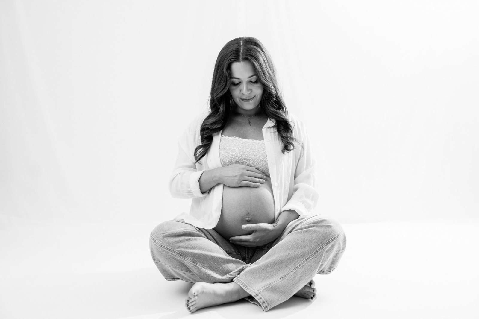 Pregnant mom sitting cross-legged, smiling down at her bump